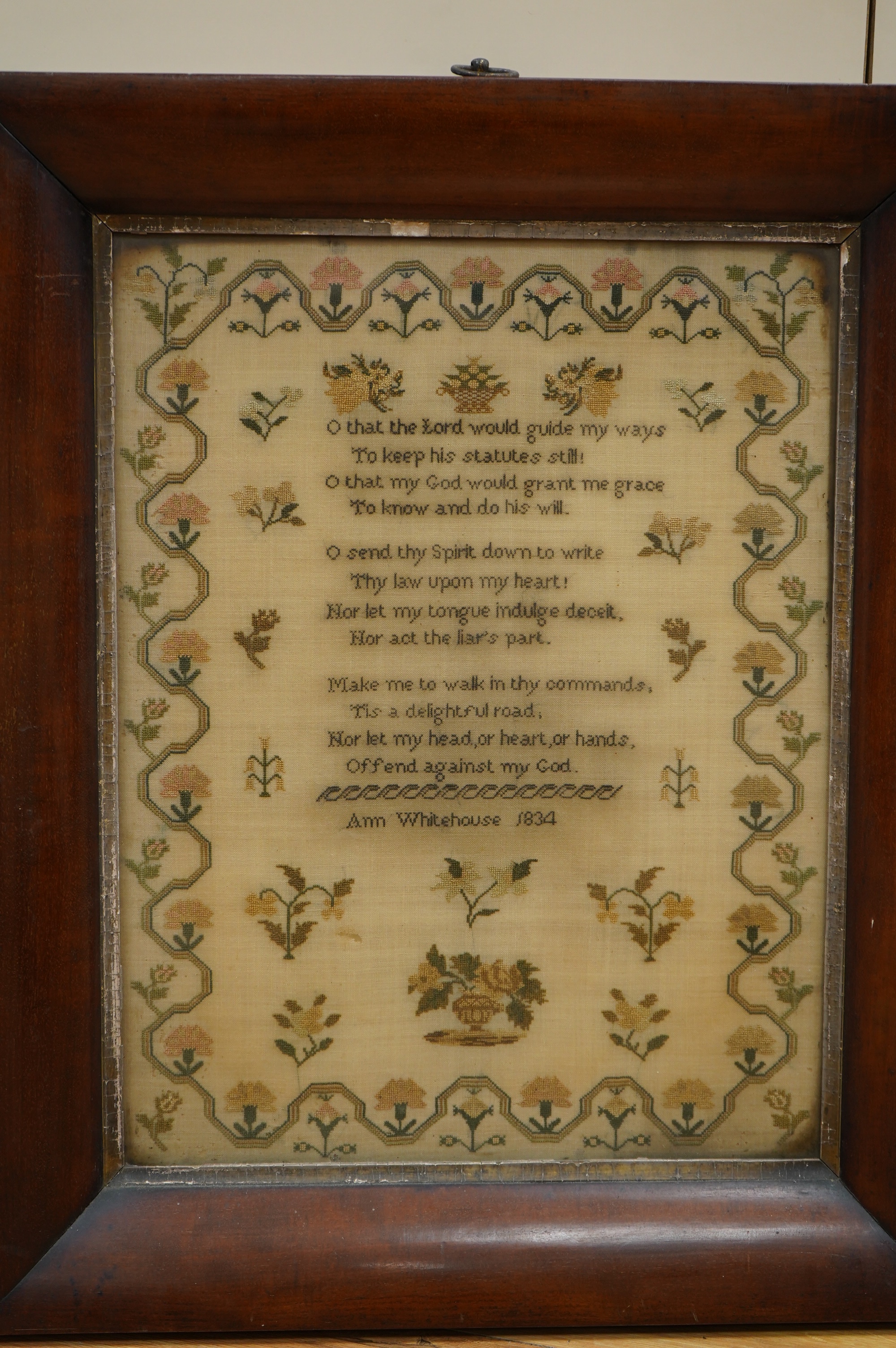 A wide mahogany framed sampler by Ann Whitehouse dated 1834, worked in coloured silks on a fine linen ground, in small stitches, bordered with a geometric stylistic vining pattern, set with a central verse, above her nam